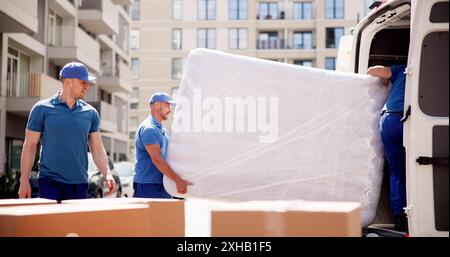 Professional Moving Services: Transportmatratze für junge Movers zur Lieferung in stolzer Arbeiteruniform am geschäftigen Tag des Unternehmens. Stockfoto
