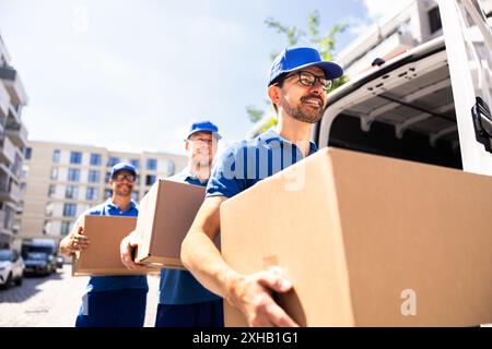 Liefermänner arbeiten zusammen, um einen Karton vor einem LKW zu transportieren. Professionelle Umsteiger, die effiziente Kurierdienste anbieten. Stockfoto