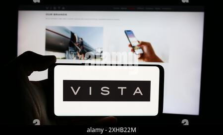 Person, die ein Mobiltelefon mit dem Logo der Emirati Aviation Company Vista Global Holding Limited vor der Webseite des Unternehmens hält. Schwerpunkt auf dem Display des Telefons. Stockfoto