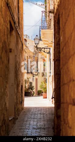 Eine bezaubernde, sonnendurchflutete Gasse in einem historischen mediterranen Dorf mit rustikalen Gebäuden, Kopfsteinpflasterpflaster und dekorativen Straßenlaternen. Stockfoto