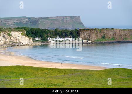 White Park Bay an der nördlichen Küste von Antrim, Nordirland. Die Basaltklippen des Giants Causeway erheben sich hinter dem Fischerdorf Portbraddan Stockfoto