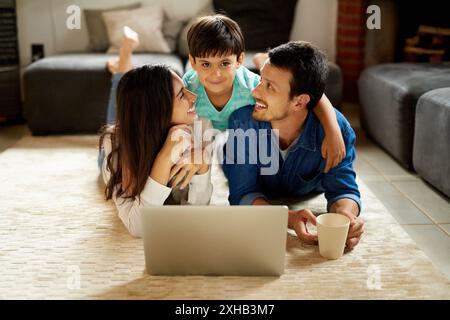 Zuhause, Paar und Kind im Porträt mit Laptop, Streaming-Film und Cartoon für Filmabend auf Teppich. Familie, Mom und Dad mit Computer zum Zuschauen Stockfoto
