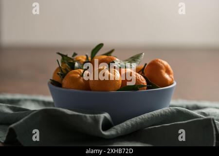 Kleine Bio-Mandarinen mit Blättern in Keramikschale auf Holztisch Stockfoto