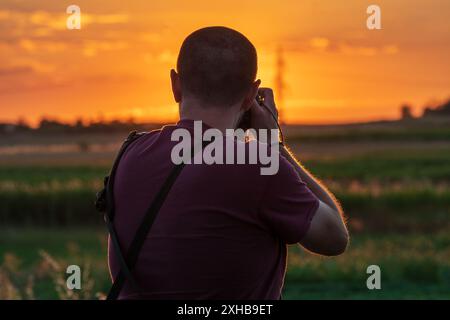 Fänger der Sonne. Fotograf, der den Sonnenuntergang einfängt, von hinten aufgenommen. Stockfoto