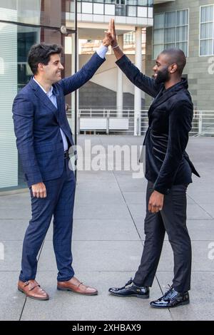 Ein vertikaler afrikanischer Geschäftsmann in einem scharfen Anzug verwickelt sich mit seinem hispanischen Gegenstück in eine freundliche Faust. Diese Geste symbolisiert multikulturelles Coll Stockfoto