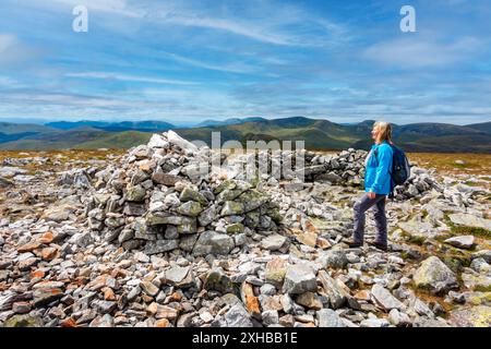 Walker am Gipfel des Cairn und Steinhügels des munro Berges Carn A Gheoidh, einer der Cairnwell Munros in Glenshee, Aberdeenshire, Schottland Stockfoto