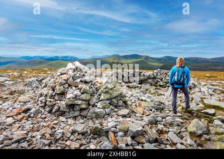 Walker am Gipfel des Cairn und Steinhügels des munro Berges Carn A Gheoidh, einer der Cairnwell Munros in Glenshee, Aberdeenshire, Schottland Stockfoto