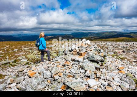 Walker am Gipfel des Cairn und Steinhügels des munro Berges Carn A Gheoidh, einer der Cairnwell Munros in Glenshee, Aberdeenshire, Schottland Stockfoto