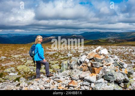 Walker am Gipfel des Cairn und Steinhügels des munro Berges Carn A Gheoidh, einer der Cairnwell Munros in Glenshee, Aberdeenshire, Schottland Stockfoto