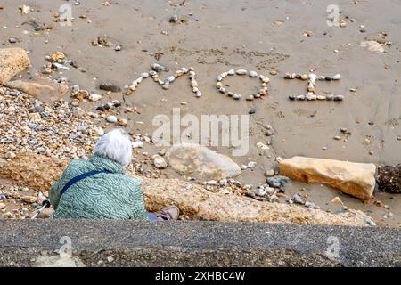 Ältere Dame, die allein am Strand auf der isle of wight sitzt. Stockfoto