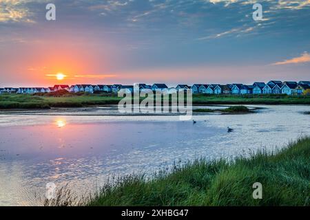 Sonnenaufgang in der Mudeford Sandspit Lagoon mit den Strandhütten auf der Mudeford Spit in der Ferne, Dorset, England Stockfoto