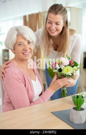 Tochter bietet ihrer erwachsenen Mutter frisch geschnittene Blumen an Stockfoto