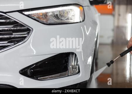 Modernes SUV-Auto mit Scheinwerferoptik an der Waschanlage. Autopflege und Waschen in einer Autowaschanlage Stockfoto