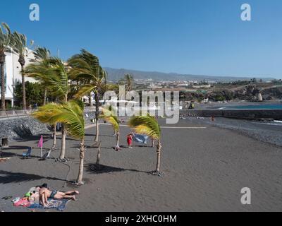 Playa de San Juan, Kanarische Insel, Teneriffa, Spanien, 1. Februar, 2024: schwarzer Sandstrand mit Sonnenbaden und kleinem Hafen. Playa de San Stockfoto