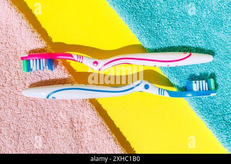 Zwei Zahnbürsten, eine rosa und eine blaue, liegen auf gelbem Hintergrund mit rosa und blauen Handtüchern. Stockfoto