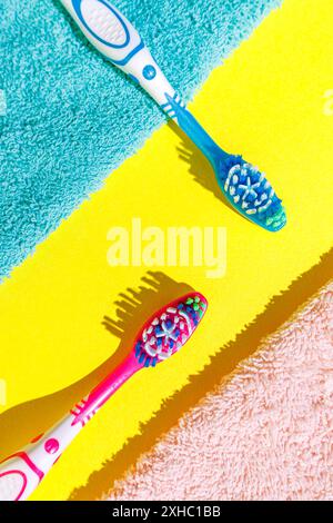 Zwei Zahnbürsten, eine blaue und eine rosa, liegen auf gelben, blauen und rosa Handtüchern. Stockfoto