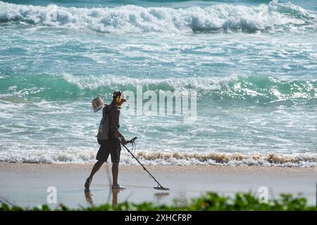 Junger Mann mit Metalldetektor, der den Sandstrand an einem sonnigen Sommertag in Phuket Thailand sucht. Schmuck am Strand mit dem Metalldetektor finden. T Stockfoto