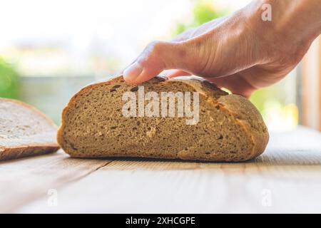 Männliche Hand hält ein frisches rustikales dunkles Brot im Freien, Frühstück Stockfoto