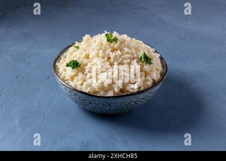 Weißer Reis, gekocht, serviert mit Petersilie, auf blauem Hintergrund Stockfoto