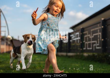 Baby-Mädchen, das mit Beagle-Hund im Garten am Sommertag läuft. Haustier mit Kinderkonzept Stockfoto