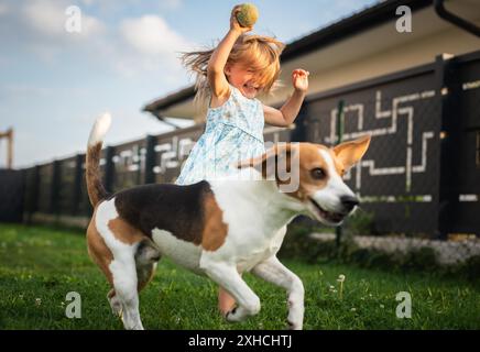 Baby-Mädchen, das mit Beagle-Hund im Garten am Sommertag läuft. Haustier mit Kinderkonzept Stockfoto