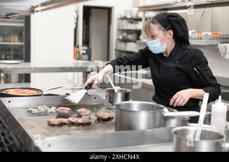 Frau Chef in Schutzmaske Gesicht bereiten Essen in der Küche eines Restaurants oder Hotels. Coronavirus-Präventionskonzept. Hochwertige Fotos Stockfoto