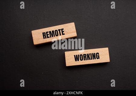 Meldung über die Fernbedienung auf Holzblöcken mit schwarzem Hintergrund. Konzeptionelles Symbol für Remote Working. Kopierbereich. Stockfoto