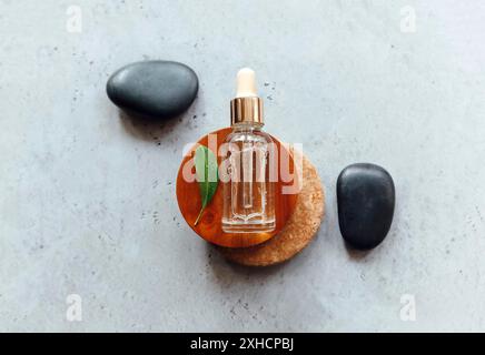 Draufsicht auf Flasche ätherisches Öl auf Holz und Stein Kreise in der Nähe von frischem Blatt und glatten Kieselsteinen platziert Stockfoto