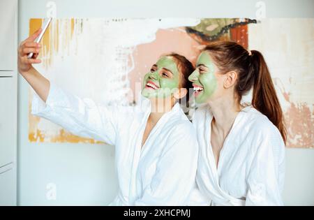 Gesellschaft von entzückten Freundinnen in Bademänteln und mit Augenflecken, die Selfie auf dem Smartphone machen, während sie sich am Wochenende im Spa-Center entspannen Stockfoto