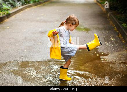 Kleines Mädchen in gelben Stiefeln und Mantel springen in regnerischen Tag Stockfoto