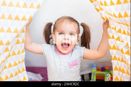 Nettes kleines Mädchen in Freizeitkleidung lachend bei der Kamera mit verschiedenen Spielzeug zu Hause Stockfoto