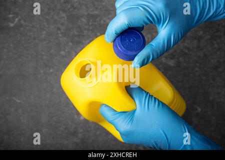 Menschliche Hand im Schutzhandschuh, die eine gelbe Bleichflasche öffnet. Desinfektionskonzept Stockfoto
