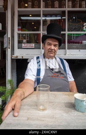 Chesham, Großbritannien. 13. Juli 2024. Ein Ladenbesitzer mit Hut bei Hats Off Chesham!, einem jährlichen Festival zum Thema Hut in Chesham, Buckinghamshire, um die historischen Verbindungen der Stadt zur Hutmacherindustrie und dem berühmten ehemaligen Residenten Roger Crabbe zu feiern. er war angeblich die Inspiration für Lewis Carrolls Mad Hatter-Figur in dem Buch Alice’s Adventures in Wonderland (auch Alice in Wonderland). Quelle: Stephen Chung / Alamy Live News Stockfoto