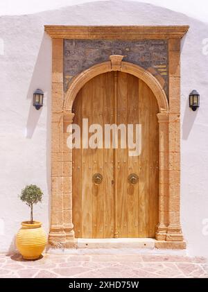 Eindrucksvolle hölzerne Eingangstür auf der griechischen Insel Hydra unter sonnigem Tageslicht. Gelbe Olivenpflanze auf der Seite. Saronischer Golf, Griechenland Stockfoto
