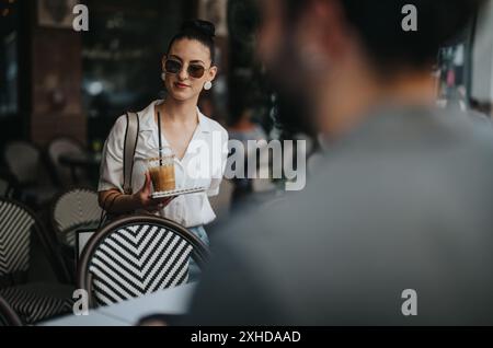 Kellnerin serviert Eiskaffee im Café mit stilvollen Stühlen mit Zebramuster Stockfoto