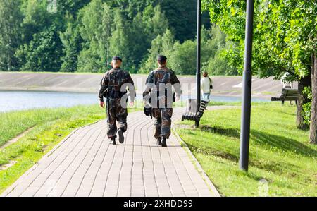 Zwei männliche Polizisten mit schwarzen Uniformen, die von hinten gesehen werden, gehen im Stadtpark und bekämpfen Verbrechen Stockfoto