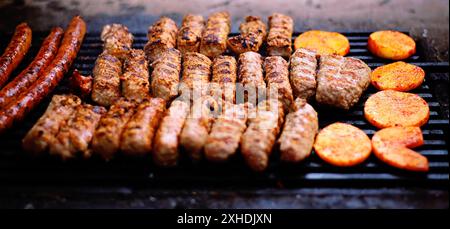 Eine Nahaufnahme gegrillter Würstchen und Kebabs mit geschnittenen Kartoffeln, die auf einem Holzkohlegrill kochen. Stockfoto