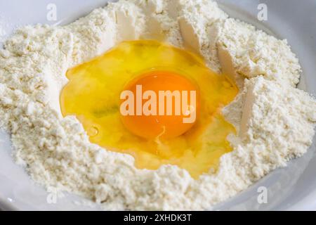 Ein einzelnes Eigelb liegt in einem Mehlbrunnen, umgeben von einem Ring mit weißem Mehl auf einer weißen Schüssel. Stockfoto