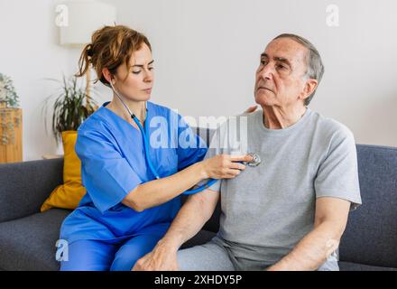 Junge Ärztin hört Herzgeräusche bei behinderter älterer Patientin zu Hause Stockfoto