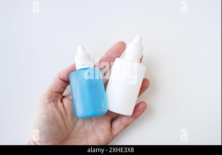 Weiße menschliche Hand, die zwei medizinische zusammendrückbare Tropfen für Glaukombehandlung hält. Kaukasier, der flüssige Arzneimittel hält. Gesundheitskonzept. Stockfoto