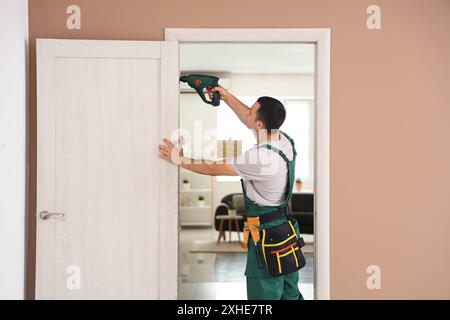 Männlicher Arbeiter mit Elektrobohrer, der die Tür zu Hause repariert Stockfoto