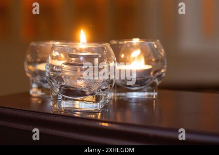 Drei Glaskerzen auf Holztisch mit warmem Hintergrund aus nächster Nähe Stockfoto