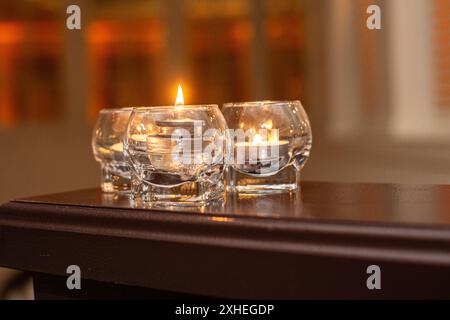 Drei Glaskerzen auf Holztisch mit warmem Hintergrund Stockfoto