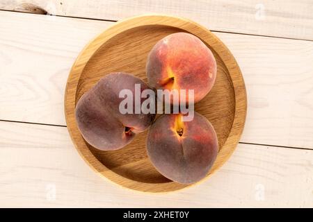 Drei reife Pfirsiche mit einem Holzteller auf einem Holztisch, Makro, Draufsicht. Stockfoto