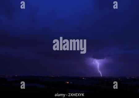 Ein Gabelbolzen trifft in der Entfernung auf den Boden. Die Lichter der Stadt sind sichtbar. Es ist Abend oder Dämmerung und wird dunkel. Das Saphirblau des Himmels. Stockfoto
