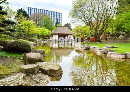 Teehaus im Japanischen Garten im Hamburger Stadtpark Planten um Blomen, Deutschland. Kleiner Teich mit Steinen. Leute auf der Holzterrasse. Stockfoto