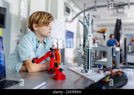 Porträt eines Schuljungen, der Roboterarm und Hand aussieht, Roboterclub nach der Schule. Kinder, die Robotik in der Grundschule lernen. Wissenschaft für Kinder. Stockfoto