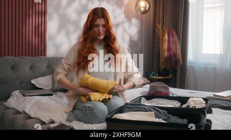 Glückliche lächelnde Frau Mädchen Frau im Schlafzimmer Hotel bereiten Sie sich auf Reise Urlaub Reise Reise Tourismus touristische Vorbereitung Tuch in Koffer Tasche Stockfoto