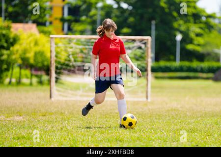 Kind spielt Fußball. Kinder spielen Fußball auf dem Platz im Freien. Teenager-Mädchen, das im Sommerpark Ball tritt. Gesunde Aktivität für Kleinkinder. Schulsport Stockfoto