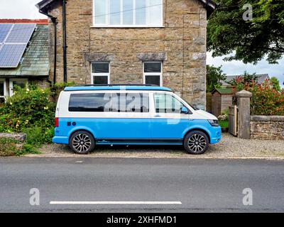 Arnside Cumbria UK. Ein blau-weißer VW-Wohnmobil parkt neben einem rustikalen Steinhaus an einer ruhigen Landstraße. Stockfoto